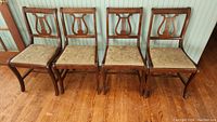 Four wooden shield back chairs arranged side by side against a paneled wall, showing overall condition and seat upholstery.