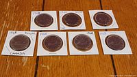 Seven 1968 Canadian silver dollar coins each mounted in individual white cardboard coin holders, handwritten labels apparent.