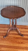 Full view of antique wooden side table showing scalloped oval top and turned legs on hardwood floor.