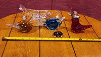 Full lot of five glass animal figurines displayed on wooden table with measuring tape for scale.