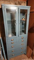 Full front view of light blue metal cabinet showing glass doors and drawer section