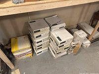 Stack of multiple boxed tile sets, some white and grey labelled Enigma, others yellow and white labeled Romamuro with measurement details.