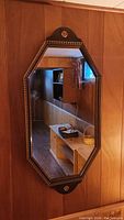 Full view of octagonal mirror mounted on wood panel wall. Shows mirror shape, frame color, and general condition.