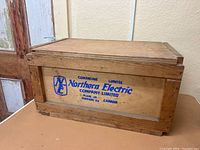 Side view showing blue printed Northern Electric logo and text on wooden crate.