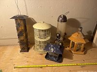 Photo showing all seven bird feeders arranged on a wooden surface against a beige wall with a measuring tape in front showing size reference.