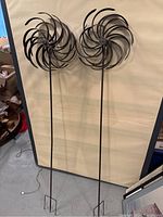 Full view of two metal windmill lawn ornaments standing upright with beige background.