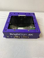 Top and front view of BrightSign 4K media player showing large heat sink and multiple serial and audio ports.