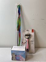Photo of the electronic cat toy box, ribbon cat wand in plastic packaging, and pink cat hair brush in sealed retail packaging.