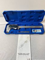 Electronic digital caliper in molded blue case alongside operating instructions.