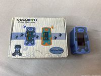 Volueth branded pulse oximeter and product box with paw print and bear graphics, blue and orange color options shown on box