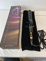 Wide shot showing the curling iron laid out on its black branded velvet pouch next to the original box with colorful streaked design and brand name 'Lumines'.