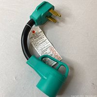 Heavy-duty EV charger adapter green plug and cable end showing 3-prong grounded plug and attached label with warnings.