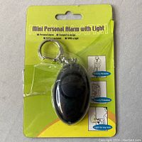 Photo of the packaged Mini Personal Alarm with Light keychain device, showing front of packaging and alarm device in plastic shell.