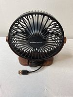 Front view of Sweetfull USB fan with protective cage and wooden base, USB cable visible.