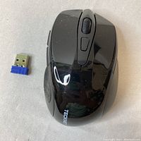 Top view of the black TECKNET wireless USB mouse and USB nano receiver placed on a white surface, showing the scroll wheel and buttons on the mouse with clear TECKNET branding.