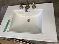 Top-down view of white rectangular bathroom sink with silver metal taps and slight dirt marks.