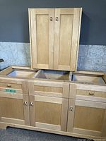 Front view of light blonde bathroom vanity base (two drawers, three doors) with matching two-door wall cabinet