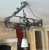 Full view of the hanging cast iron pot holder with grapevine decoration and multiple hooks.