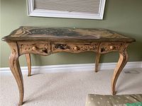 Front view of French Provincial floral painted library table showing curved legs and painted floral motifs on top and sides, table positioned against wall with carpet floor.