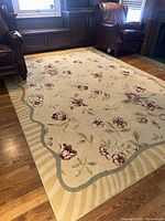 Area rug fully visible in room between two leather chairs on hardwood floor, showing floral pattern and scalloped border detail.