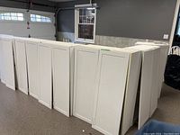 Six white shaker style wall cabinets standing upright on garage floor.