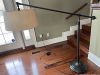 Full side view of the adjustable floor lamp showing cream shade, horizontal arm and round weighted base.