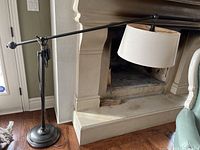 Full view of floor lamp showing weighted round base, straight stem, adjustable horizontal arm, and fabric drum shade