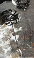Two metal pinwheels laid on ground showing spiral blades and long stakes, one stake bent.