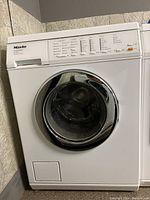 Full view of white front-loading washing machine with chrome circular door and control panel showing various program options.