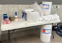 Table top with various packing materials including bubble wrap rolls, tape, foam sheets, tissue paper, and plant tags
