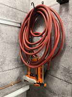 Full view of the orange Paslode framing nailer mounted on the wall with coiled red hose connected.