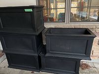 Five black rectangular planters stacked outside against stone wall and window.