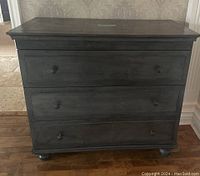 Front view of charcoal-finish three-drawer dresser with round metal knobs and bun feet.