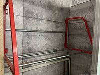 Full view of metal tire rack showing red frame and three horizontal silver rods mounted against concrete wall.