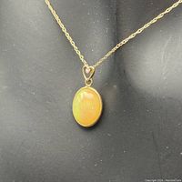 Close-up of the faux opal pendant attached to the 14k gold chain with small heart-shaped detail and stone.