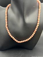 Front view of the vintage coral bead necklace displayed on a black bust, showing the smooth round beads and length of 16 inches.