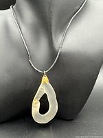Necklace with translucent stone pendant displayed on black mannequin bust showing pendant shape and color.
