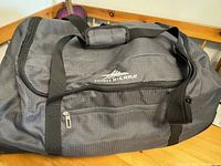 Front view of black High Sierra duffel bag with handles and zippered front pocket.