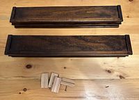 Two dark stained wooden floating shelves with mounting blocks and screws, simple rectangular design.