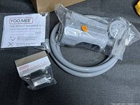 Photo of handheld shower sprayer, hose, and quick connect tub spout diverter fitting in plastic bags with instruction manual