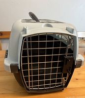 Front view of gray and brown plastic pet carrier showing metal wire door with latch.