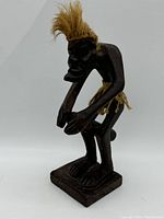 Side angle showing drumming pose, handcarved detail and grass hair on wooden figurine.