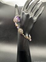 Full view of purple amethyst and silver tone handmade bracelet on display hand form showing the length and curve of beads and metal filigree spacers.