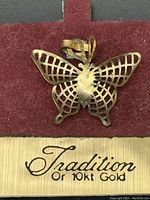 Close-up of the back of the butterfly pendant showing openwork detailing and the gold card with the Tradition brand name and gold purity mark.