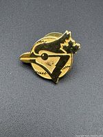 Front view of vintage original Toronto Blue Jays pinback with gold tone and black enamel on circular baseball background, slight scuff on cheek of blue jay.