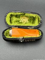 Close-up of amber cheroot holder inside green velvet-lined fitted case with gold emblem in lid