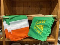 Photo showing a grouping of Irish tricolor flags and 'Erin Go Bragh' flags with wooden sticks on a wooden shelf.