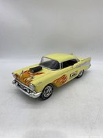 Front side view of yellow 1957 Chevrolet hot rod decanter with flame artwork and black engine blower on hood.