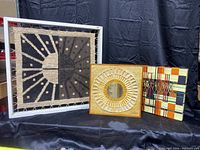 Front view of all three mid century textile art pieces displayed against a black backdrop.
