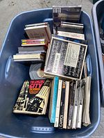 Top view of the plastic bin showing CDs in jewel cases, cassette tapes, booklets and film reels.